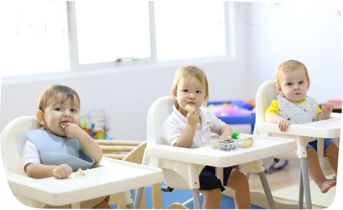 Babies seated in high chairs enjoying mealtime at Step by Step Nursery Dubai, promoting social interaction and sharing skills.