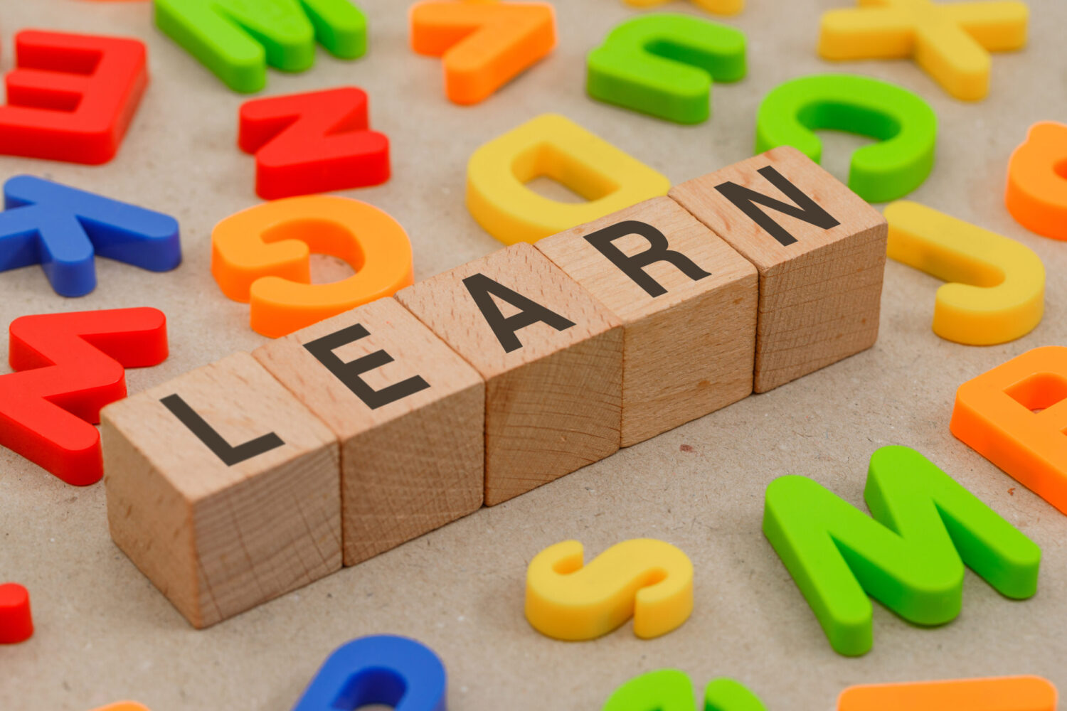 A child's set of wooden blocks with letters spelling out the word "learn" appear among coloured plastic letters