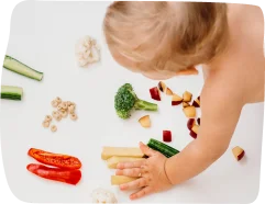 A toddler exploring vegetables like broccoli, cucumber, and red peppers during a sensory learning activity, with Step By Step Nursery Dubai promoting healthy eating habits through interactive experiences.